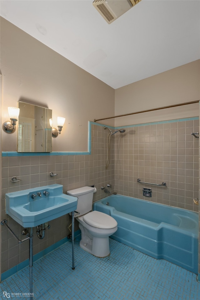 full bathroom with tile walls, toilet, tiled shower / bath combo, tasteful backsplash, and tile flooring