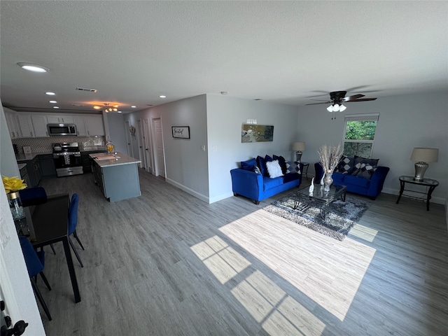 living room featuring ceiling fan, a textured ceiling, and light hardwood / wood-style floors