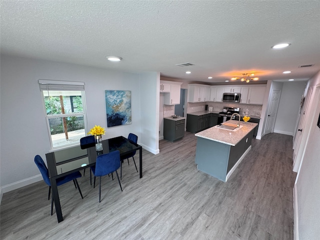 kitchen featuring light wood-type flooring, backsplash, white cabinetry, a center island with sink, and stainless steel appliances