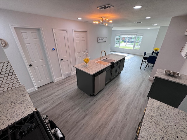 interior space featuring hardwood / wood-style floors, stainless steel dishwasher, a chandelier, sink, and an island with sink