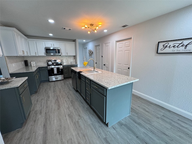 kitchen with appliances with stainless steel finishes, light hardwood / wood-style floors, white cabinetry, and an island with sink