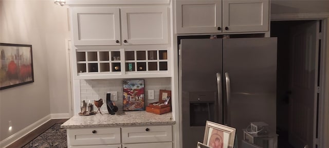 kitchen with backsplash, white cabinets, dark hardwood / wood-style floors, stainless steel fridge, and light stone counters