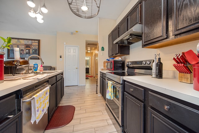 kitchen with stainless steel appliances, wall chimney exhaust hood, dark brown cabinets, sink, and pendant lighting