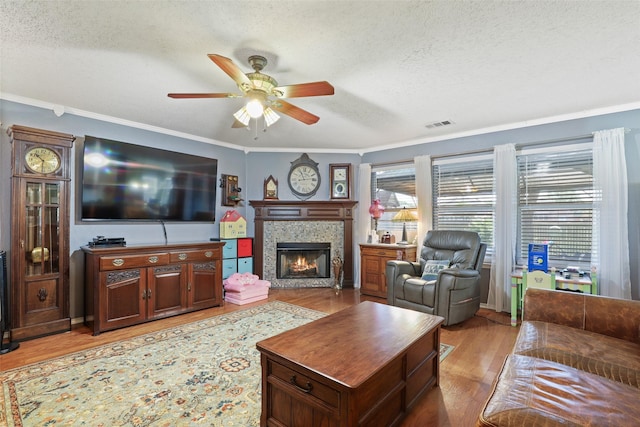 living room with a tile fireplace, crown molding, a textured ceiling, and light wood-type flooring