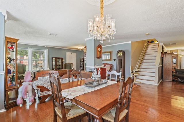 dining space featuring crown molding, wood-type flooring, a textured ceiling, and an inviting chandelier