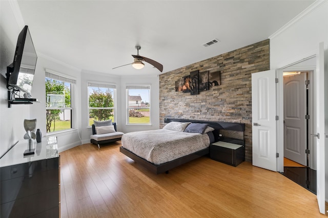 bedroom featuring ornamental molding, ceiling fan, light wood-type flooring, and a fireplace