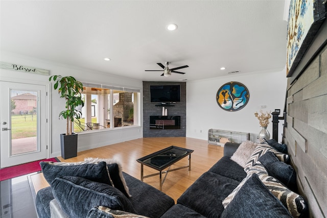 living room with a large fireplace, ceiling fan, hardwood / wood-style floors, and ornamental molding