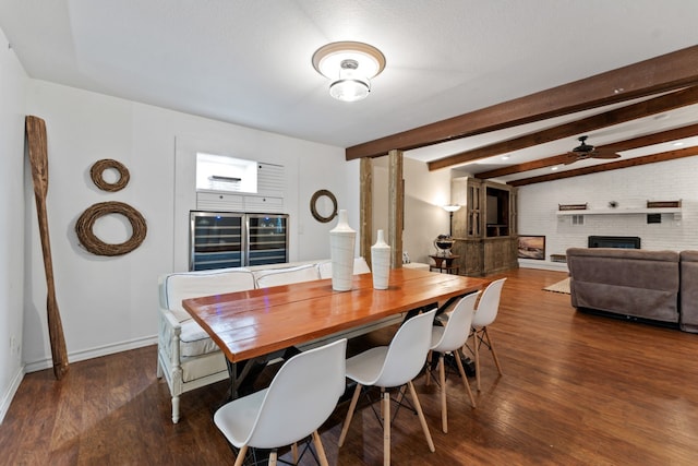 dining space featuring brick wall, dark hardwood / wood-style floors, ceiling fan, a brick fireplace, and beam ceiling