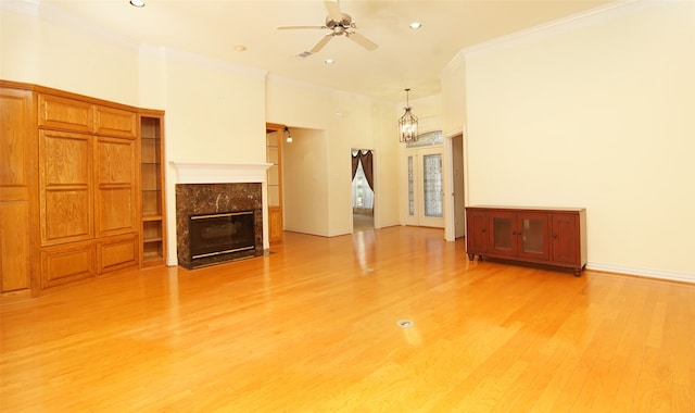 unfurnished living room featuring a high end fireplace, light wood-type flooring, ceiling fan with notable chandelier, and crown molding