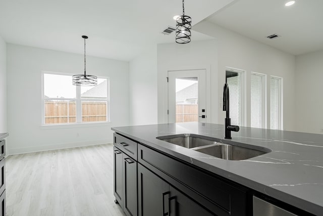 kitchen with an inviting chandelier, light hardwood / wood-style floors, stone countertops, sink, and pendant lighting