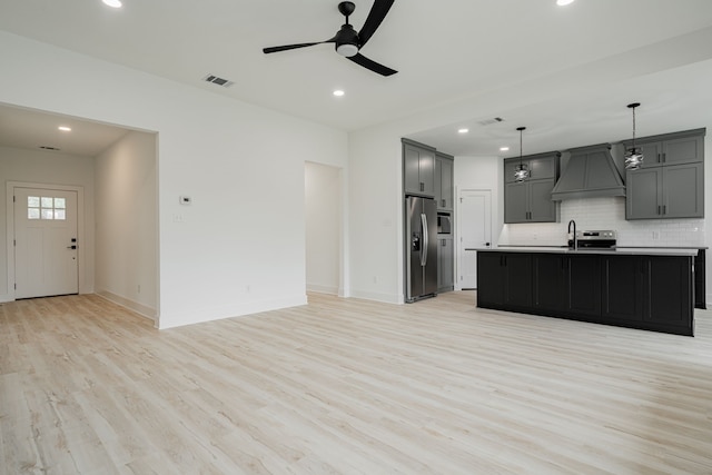 kitchen featuring light wood-type flooring, appliances with stainless steel finishes, an island with sink, premium range hood, and ceiling fan