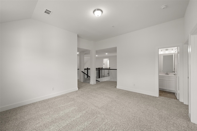 unfurnished bedroom with sink, vaulted ceiling, light colored carpet, and ensuite bath