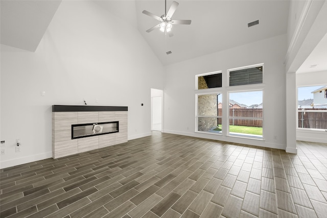 unfurnished living room featuring ceiling fan, high vaulted ceiling, a tiled fireplace, and wood-type flooring