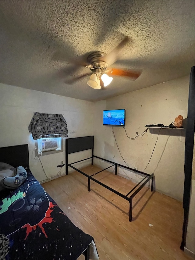 bedroom with a textured ceiling, wood-type flooring, ceiling fan, and a wall mounted air conditioner