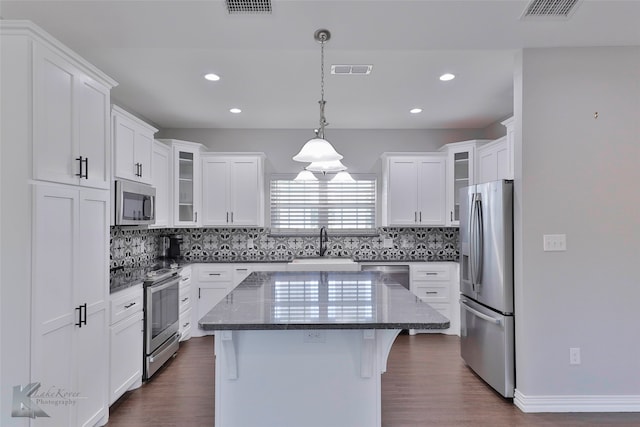 kitchen with dark hardwood / wood-style floors, tasteful backsplash, stainless steel appliances, a center island, and a kitchen bar