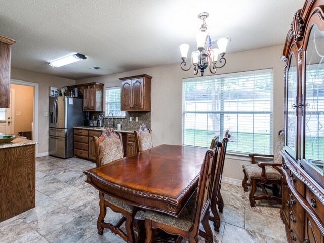 dining space featuring a notable chandelier, sink, light tile flooring, and a healthy amount of sunlight