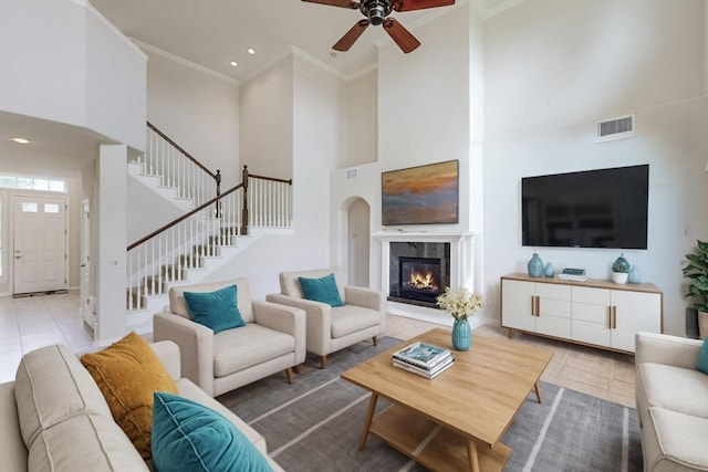 living room with light tile patterned floors, ornamental molding, a towering ceiling, and ceiling fan