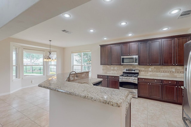 kitchen featuring a notable chandelier, stainless steel appliances, backsplash, and a center island with sink