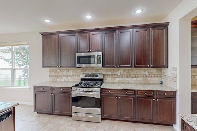 kitchen with light stone counters, backsplash, light tile patterned floors, stainless steel appliances, and dark brown cabinetry