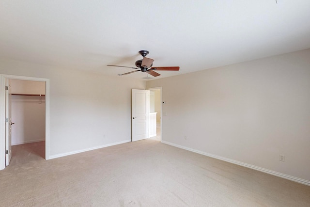 unfurnished bedroom with a closet, light colored carpet, ceiling fan, and a walk in closet