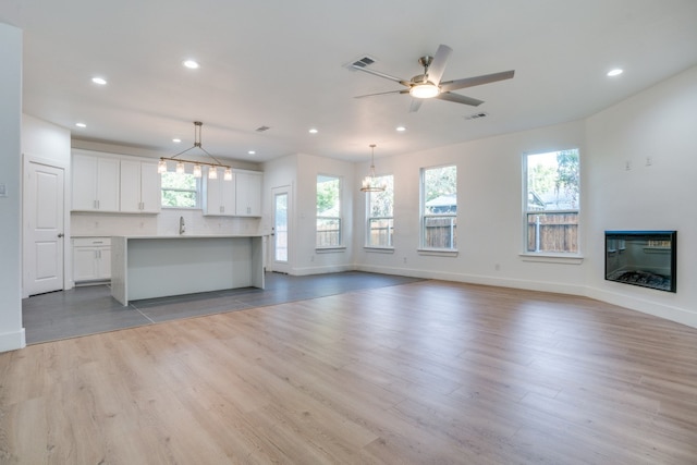 unfurnished living room featuring sink, ceiling fan with notable chandelier, and light hardwood / wood-style flooring