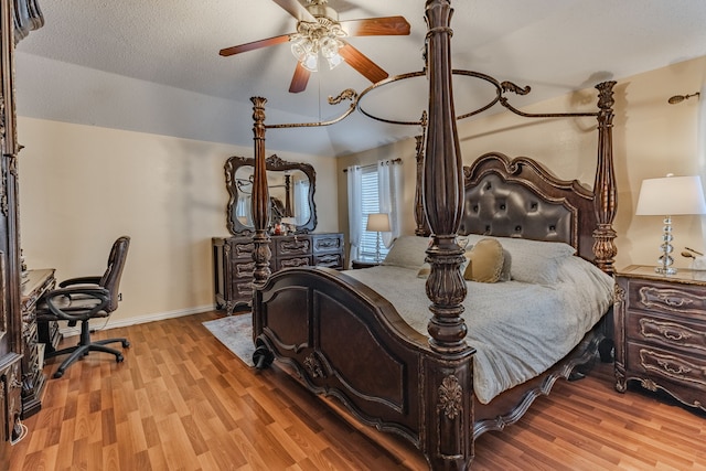 bedroom with ceiling fan, a textured ceiling, light wood-type flooring, and vaulted ceiling