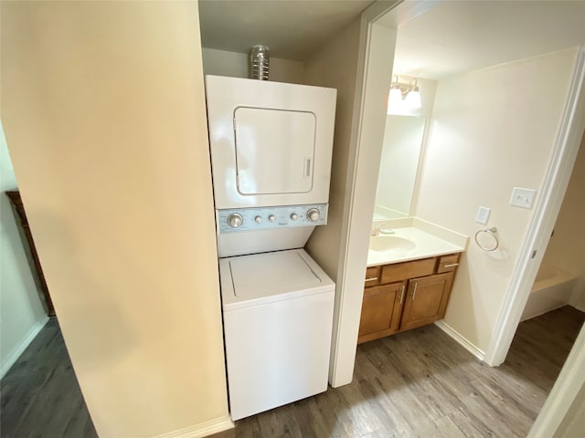 clothes washing area with sink, stacked washing maching and dryer, and hardwood / wood-style flooring