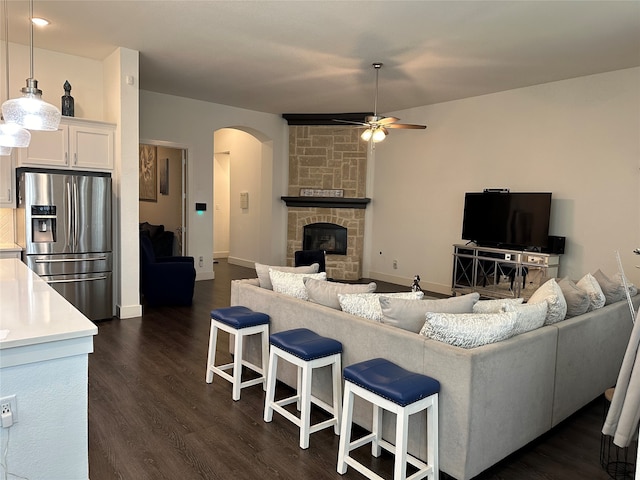 living room with a stone fireplace, ceiling fan, and dark hardwood / wood-style floors