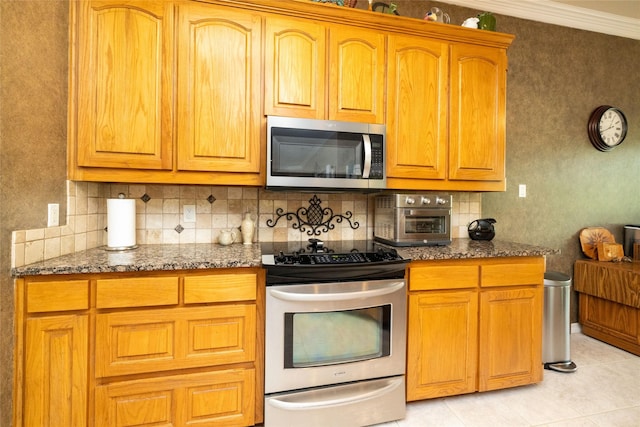 kitchen featuring light tile patterned flooring, crown molding, stainless steel appliances, and dark stone counters