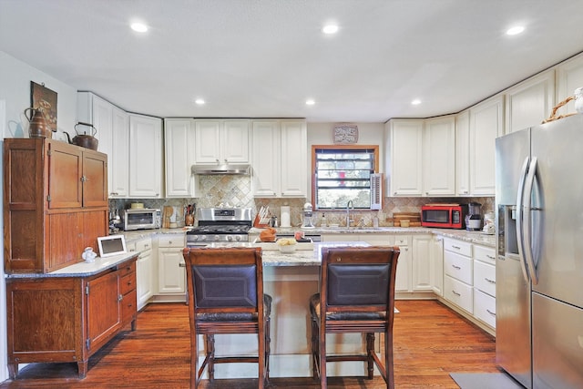 kitchen with light stone countertops, stainless steel appliances, white cabinets, dark hardwood / wood-style floors, and a kitchen island