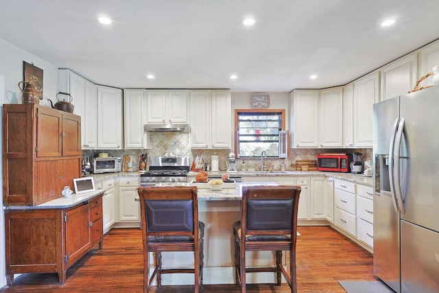 kitchen with appliances with stainless steel finishes, a sink, under cabinet range hood, a kitchen island, and dark wood finished floors