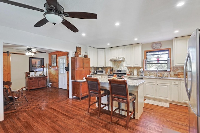 kitchen with stainless steel appliances, a sink, wood finished floors, white cabinets, and recessed lighting