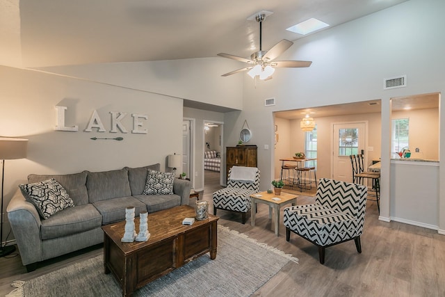 living room featuring a skylight, ceiling fan, high vaulted ceiling, and wood-type flooring