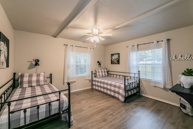 bedroom featuring beamed ceiling, hardwood / wood-style floors, multiple windows, and ceiling fan