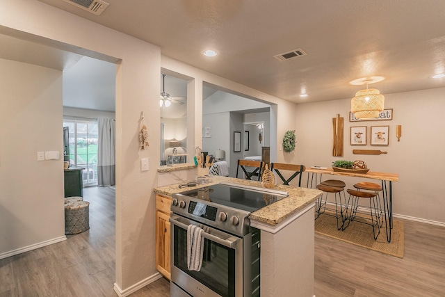 kitchen featuring kitchen peninsula, light stone countertops, light wood-type flooring, stainless steel range, and ceiling fan