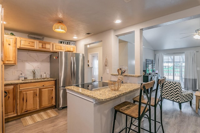 kitchen with stainless steel refrigerator, sink, a center island, decorative backsplash, and light wood-type flooring