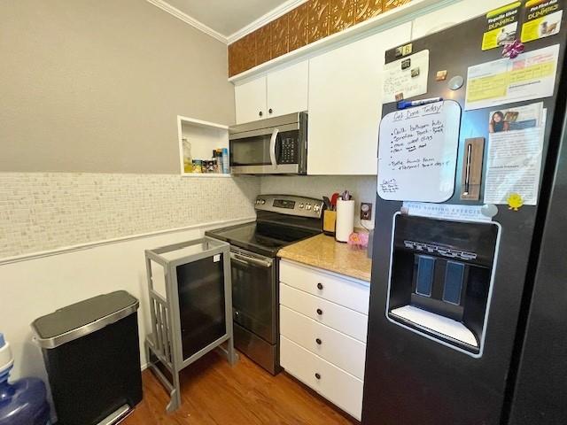 kitchen with dark hardwood / wood-style flooring, stainless steel appliances, white cabinetry, and crown molding