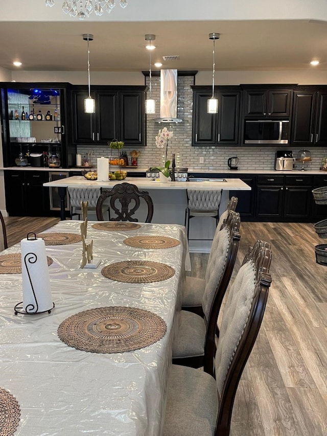 kitchen featuring wall chimney range hood, hardwood / wood-style floors, pendant lighting, a breakfast bar area, and decorative backsplash