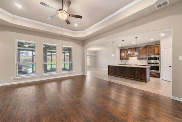 unfurnished living room featuring ceiling fan with notable chandelier, light hardwood / wood-style flooring, ornamental molding, and sink