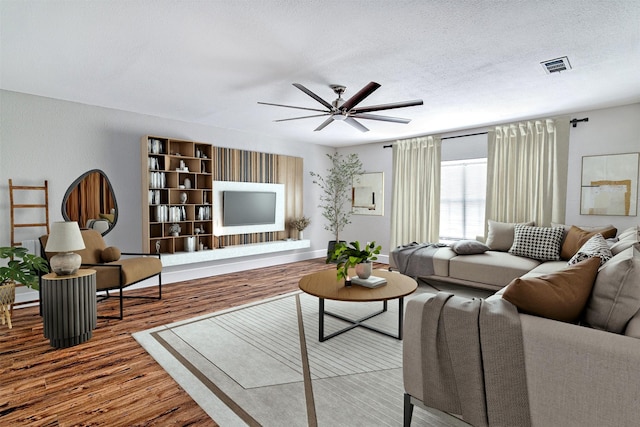 living room featuring ceiling fan, hardwood / wood-style flooring, and a textured ceiling