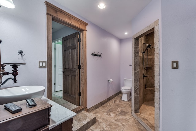 bathroom featuring a tile shower, vanity, toilet, and tile floors