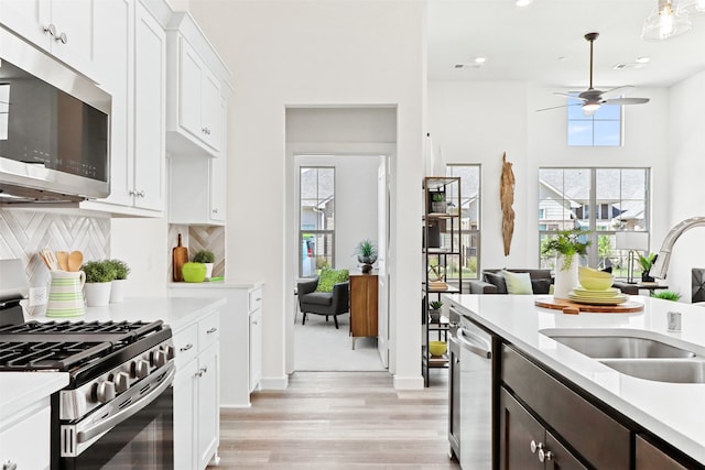 kitchen featuring light wood-type flooring, sink, backsplash, appliances with stainless steel finishes, and white cabinetry