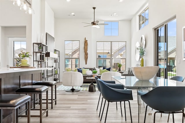 dining space with ceiling fan, light hardwood / wood-style flooring, a high ceiling, and a healthy amount of sunlight