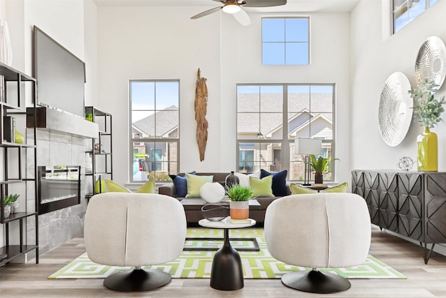 living room featuring a towering ceiling, a tile fireplace, light hardwood / wood-style flooring, and ceiling fan