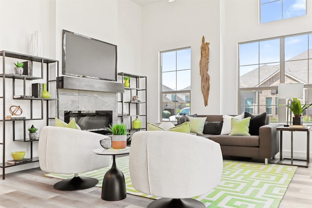 living room featuring light wood-type flooring, a tiled fireplace, a high ceiling, and a healthy amount of sunlight