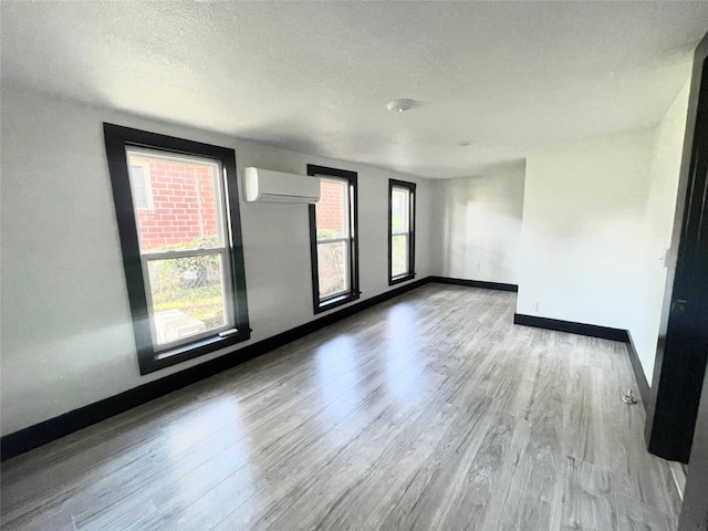 empty room with a wall unit AC, light hardwood / wood-style floors, and a textured ceiling