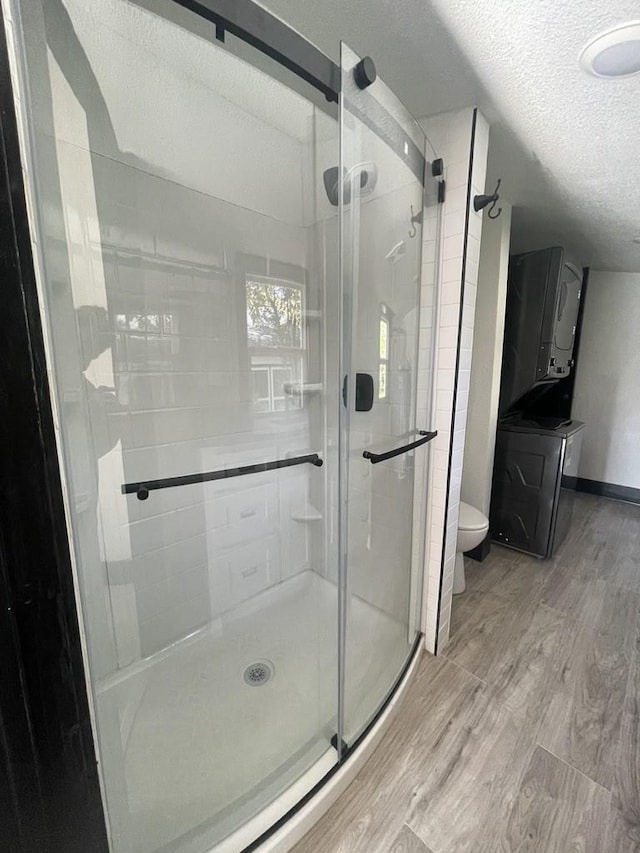 bathroom with a textured ceiling, hardwood / wood-style floors, washer / clothes dryer, toilet, and a shower with shower door