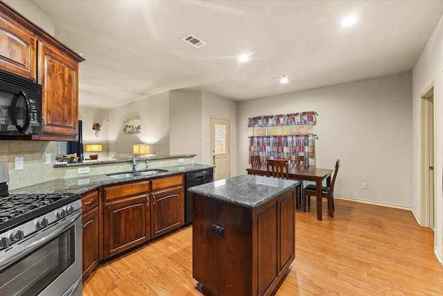 kitchen with dark stone counters, black appliances, sink, light wood-type flooring, and a kitchen island