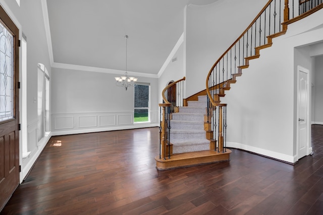 foyer entrance with ornamental molding, high vaulted ceiling, dark wood-type flooring, and an inviting chandelier