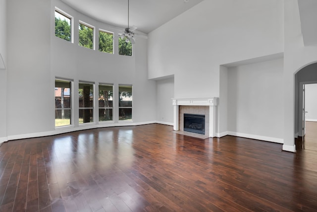 unfurnished living room with a tile fireplace, ceiling fan, hardwood / wood-style floors, and a towering ceiling